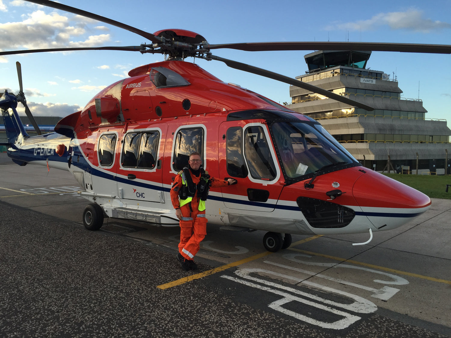 Chris, founder of Ground Effect Coffee Roasters, in orange safety suit standing next to a red helicopter on an airport tarmac