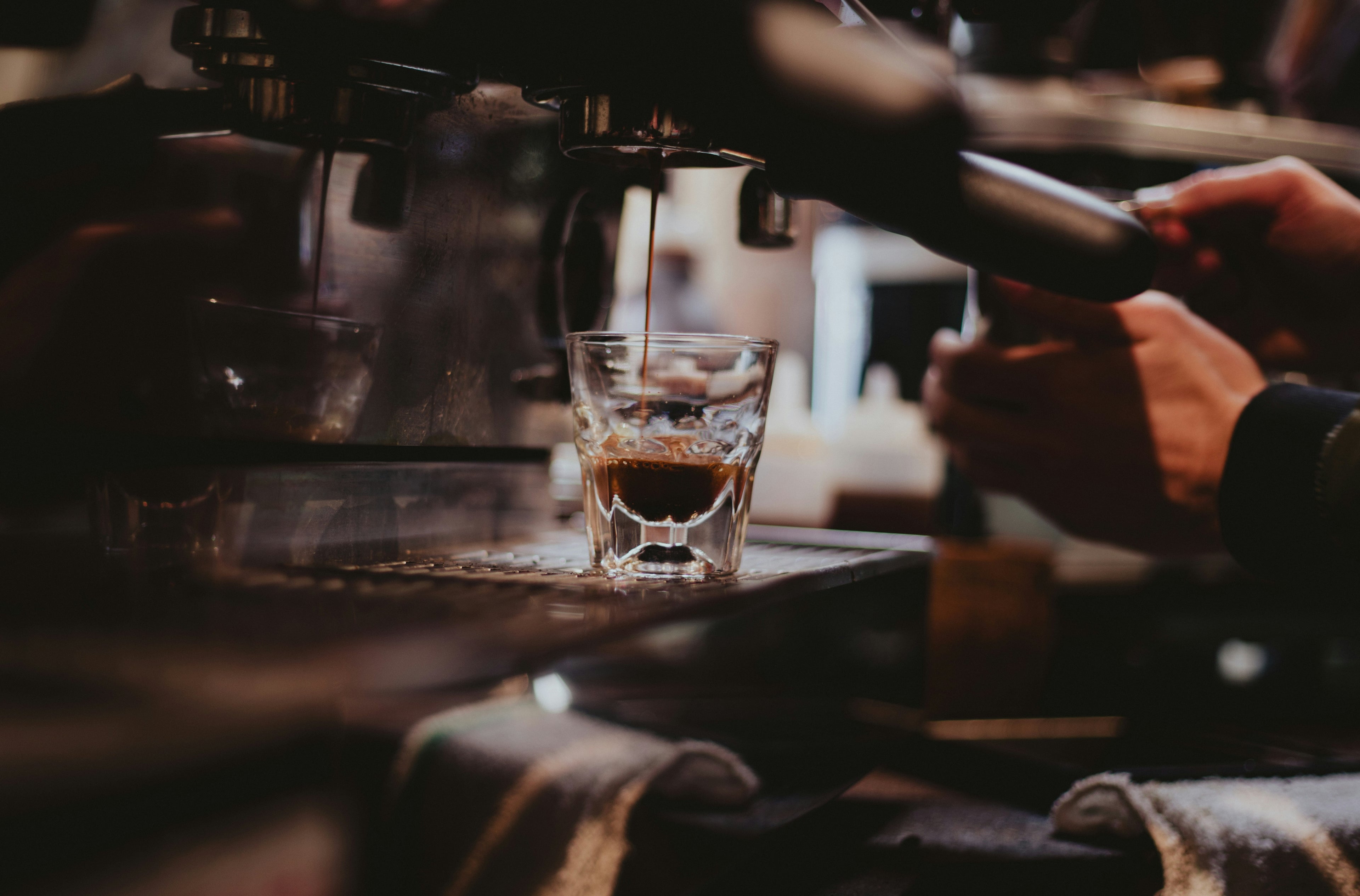 Person making a shot of espresso in a glass cup using an espresso machine.